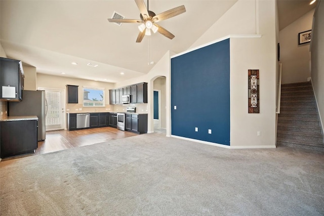 unfurnished living room featuring high vaulted ceiling, ceiling fan, arched walkways, light colored carpet, and baseboards
