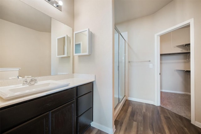 bathroom with a walk in closet, wood finished floors, vanity, and a stall shower