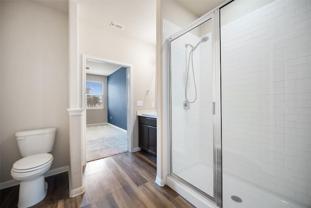 bathroom with toilet, visible vents, wood finished floors, a shower stall, and vanity