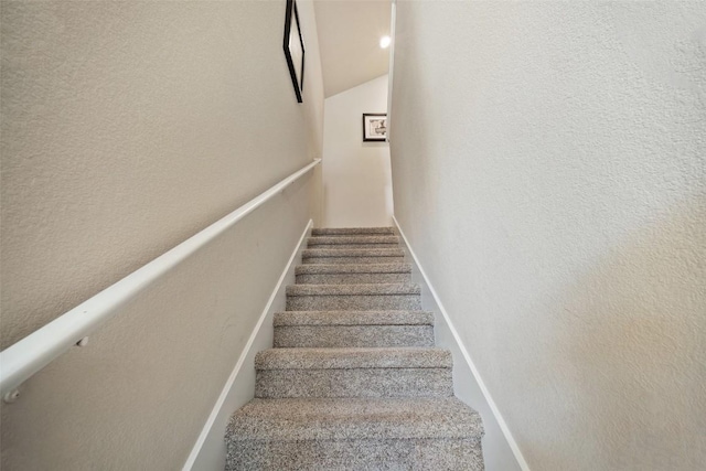 staircase featuring lofted ceiling and baseboards