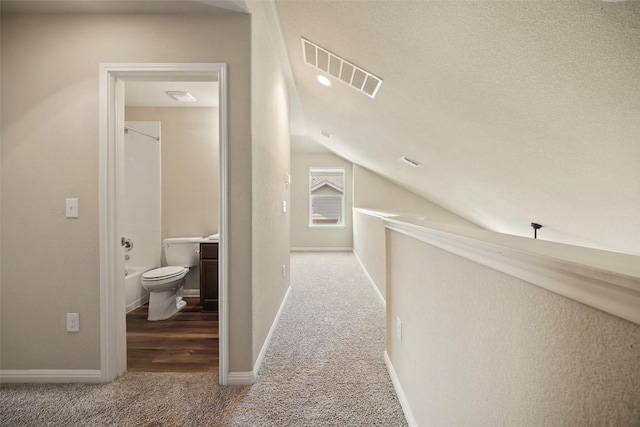 hall with vaulted ceiling, carpet floors, visible vents, and baseboards