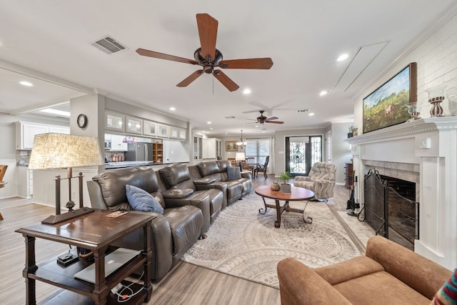 living area with a ceiling fan, a fireplace with flush hearth, light wood finished floors, visible vents, and recessed lighting