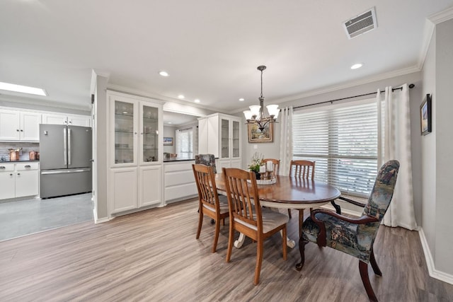 dining room with light wood-type flooring, baseboards, visible vents, a notable chandelier, and crown molding