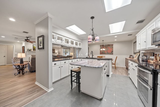 25 Doolittle Dr, Wimberley, TX 78676 - kitchen with a peninsula, appliances with stainless steel finishes, a sink, a skylight, and white cabinets