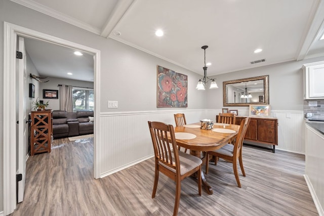 dining area featuring light wood finished floors, an inviting chandelier, visible vents, crown molding, and wainscoting