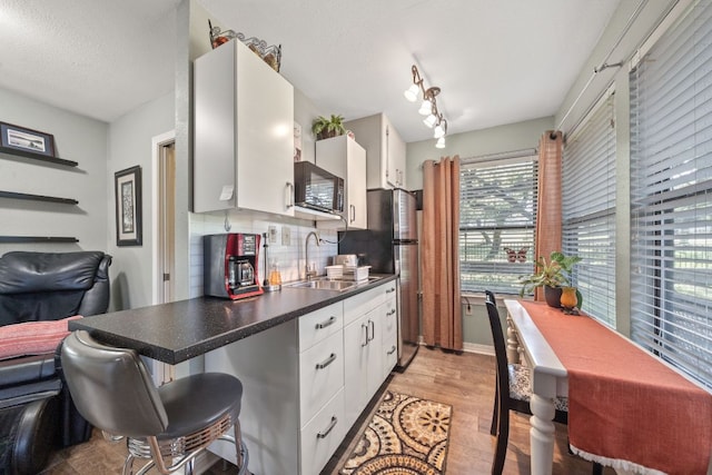 kitchen with dark countertops, tasteful backsplash, a sink, black microwave, and white cabinetry