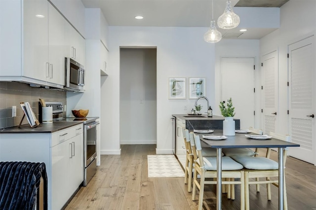 kitchen with appliances with stainless steel finishes, a sink, light wood-style flooring, white cabinetry, and recessed lighting
