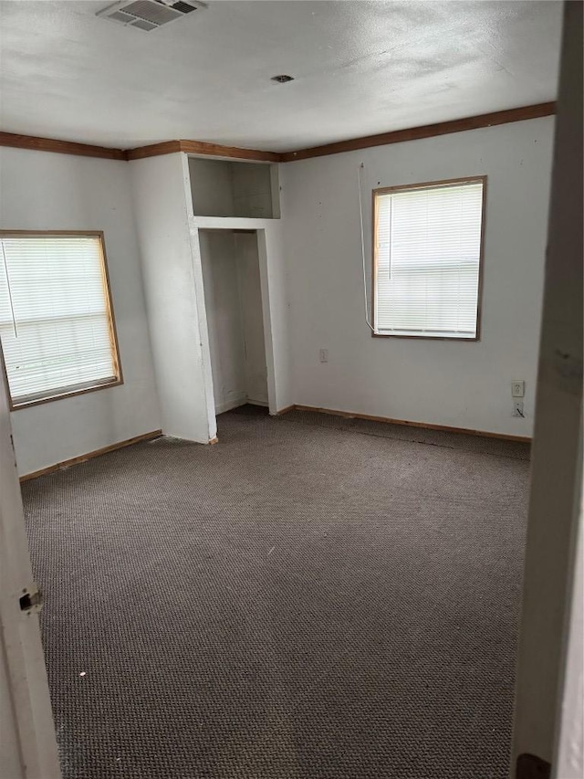 unfurnished bedroom with ornamental molding, multiple windows, visible vents, and carpet