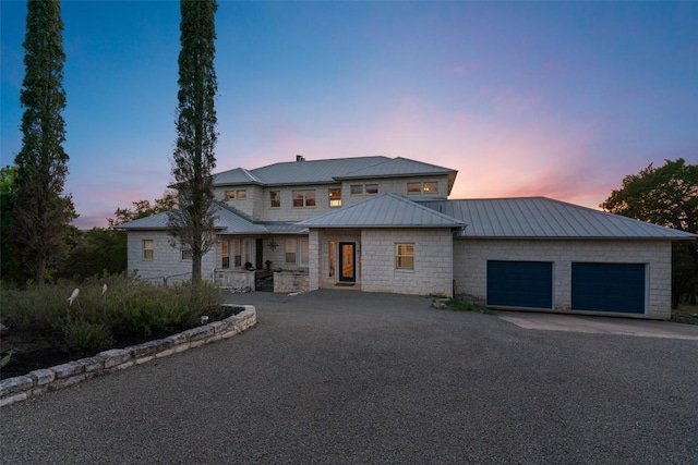 view of front of property with aphalt driveway, metal roof, a standing seam roof, stone siding, and a garage