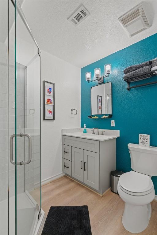 full bathroom featuring toilet, wood finished floors, visible vents, and a stall shower