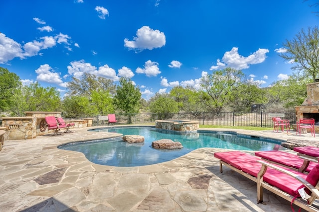 view of swimming pool with fence, an outdoor stone fireplace, a pool with connected hot tub, and a patio