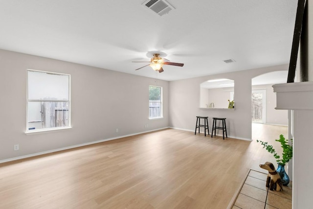 unfurnished living room with ceiling fan, arched walkways, visible vents, and light wood-type flooring