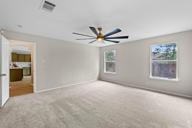 empty room featuring visible vents, arched walkways, baseboards, carpet flooring, and ceiling fan