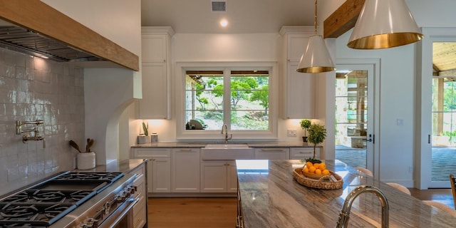 kitchen with a sink, decorative backsplash, high end range, white cabinets, and visible vents