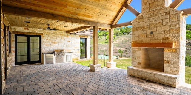 view of patio featuring grilling area, an outdoor kitchen, an outdoor stone fireplace, and a ceiling fan