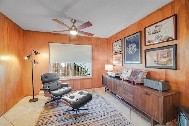 living area with light tile patterned flooring, wooden walls, and a ceiling fan