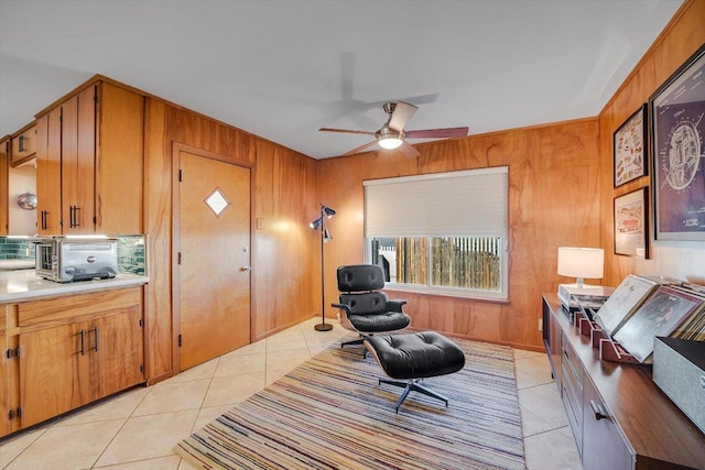 sitting room with ceiling fan, wood walls, a toaster, and light tile patterned floors