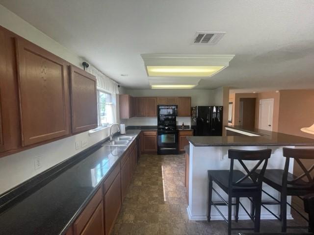 kitchen featuring a sink, a breakfast bar, stove, visible vents, and freestanding refrigerator