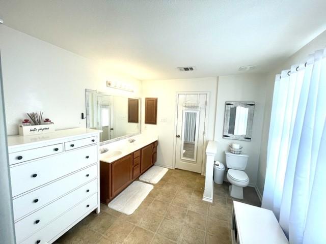bathroom with tile patterned flooring, visible vents, toilet, vanity, and a healthy amount of sunlight