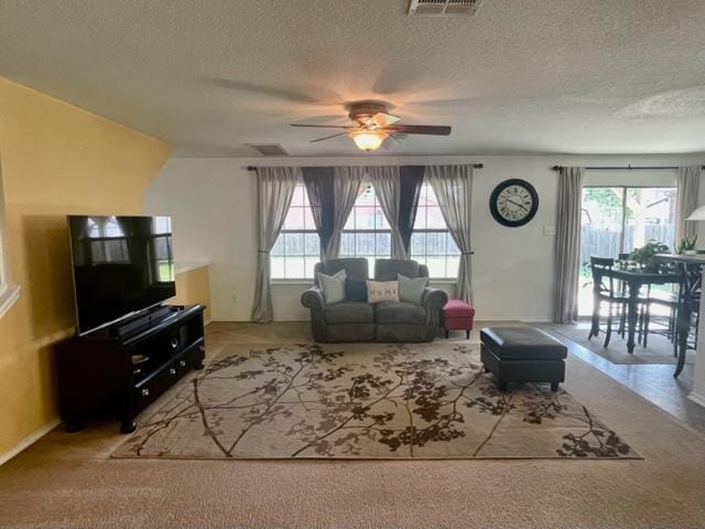 living area featuring carpet, a textured ceiling, and ceiling fan