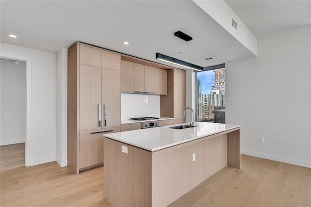 44 E Ave Unit 3107, Austin, TX 78701 - kitchen featuring a sink, light brown cabinets, light wood-style floors, light countertops, and a kitchen island with sink