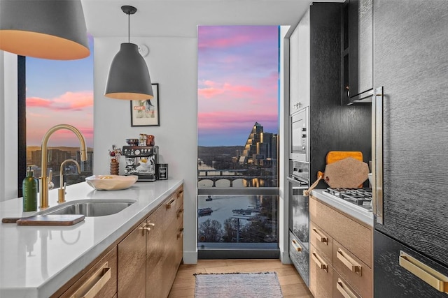 kitchen with light countertops, a sink, pendant lighting, stainless steel gas cooktop, and light wood-style flooring