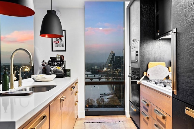 kitchen with light countertops, a sink, pendant lighting, light wood-style flooring, and gas stovetop