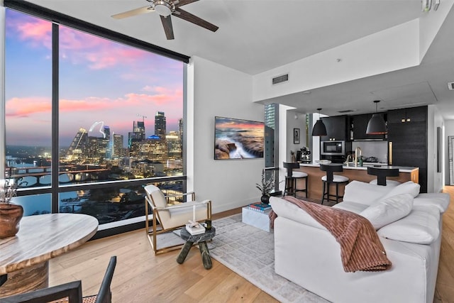 living room featuring a ceiling fan, expansive windows, a view of city, light wood-style floors, and visible vents