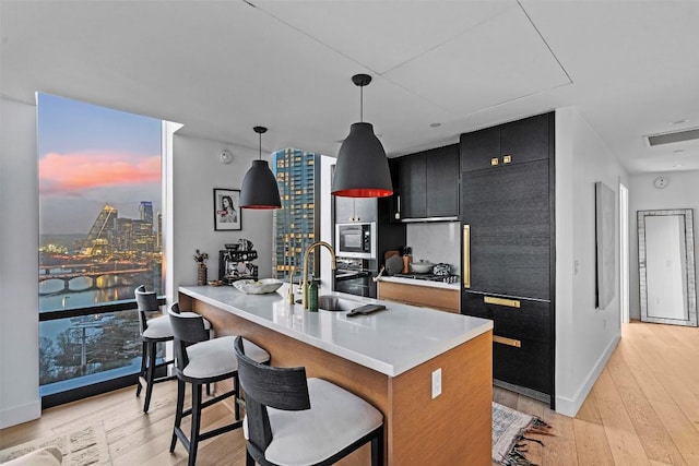 kitchen with hanging light fixtures, a breakfast bar, light wood-type flooring, appliances with stainless steel finishes, and dark cabinets