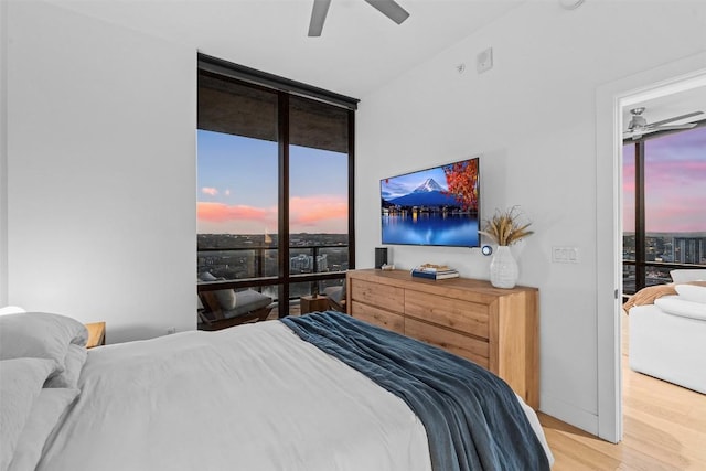 bedroom featuring light wood finished floors, floor to ceiling windows, ceiling fan, and access to exterior