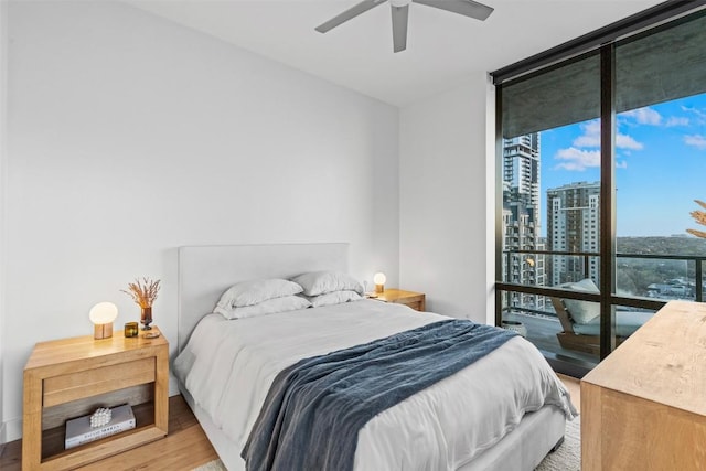 bedroom with light wood-style floors, a ceiling fan, floor to ceiling windows, access to outside, and a view of city