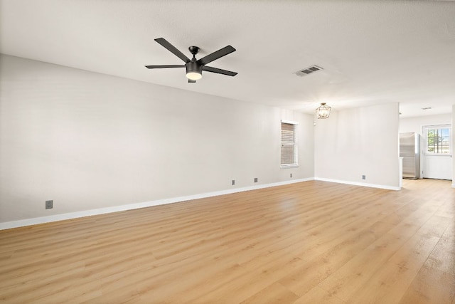 empty room with baseboards, light wood finished floors, visible vents, and ceiling fan with notable chandelier