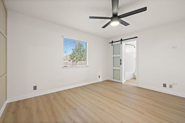 unfurnished bedroom featuring connected bathroom, a barn door, baseboards, and light wood-type flooring