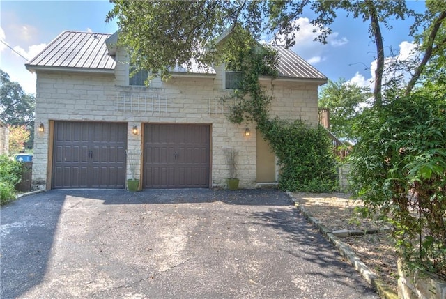 exterior space featuring a garage, stone siding, metal roof, and aphalt driveway