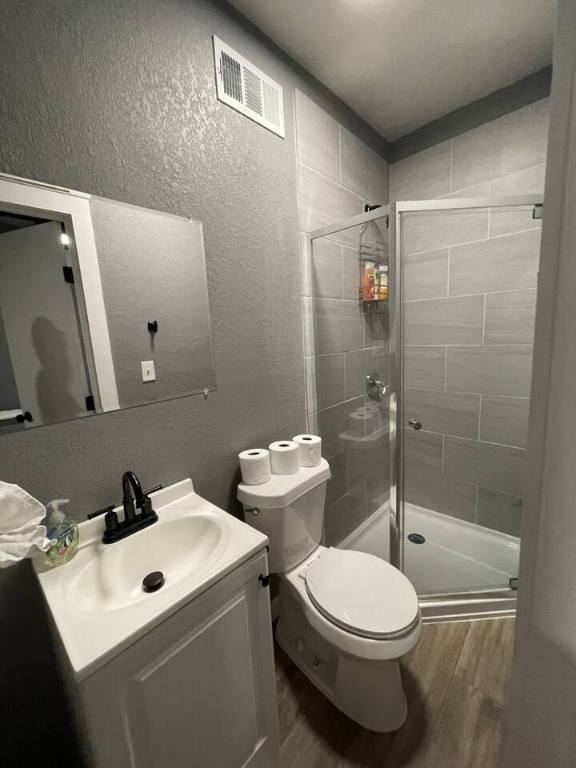 bathroom with visible vents, toilet, a textured wall, wood finished floors, and a stall shower
