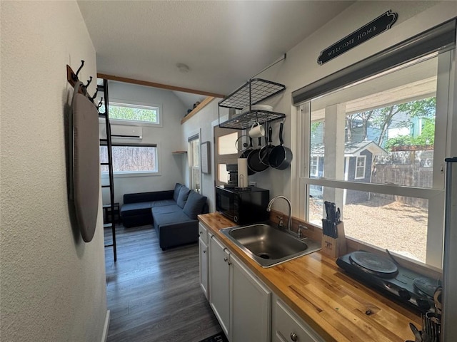 kitchen with black microwave, a wall mounted AC, a sink, butcher block countertops, and dark wood-style floors