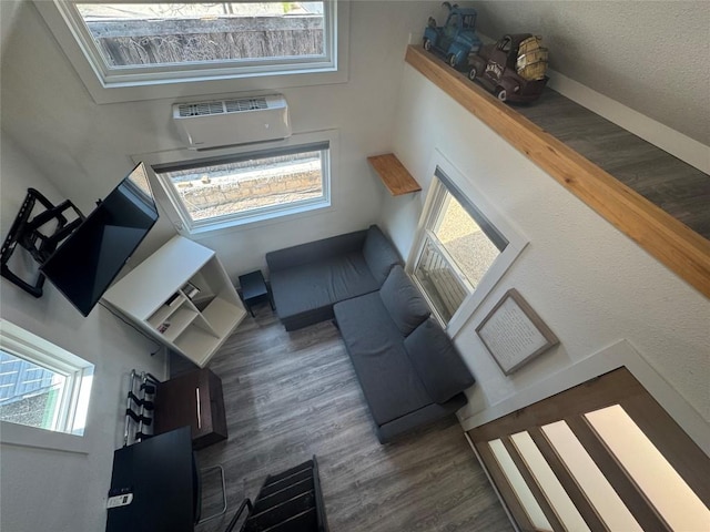 living area with a wall mounted AC, wood finished floors, and a towering ceiling