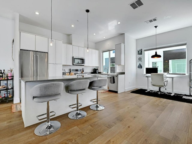 505 Tillery St Unit 6, Austin, TX 78702 - kitchen with appliances with stainless steel finishes, a breakfast bar, light wood-style floors, white cabinets, and recessed lighting