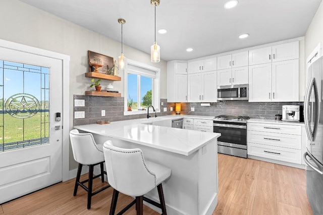 7993 W Fm 487, Florence, TX 76527 - kitchen with appliances with stainless steel finishes, a peninsula, a breakfast bar, white cabinetry, and light wood-style floors