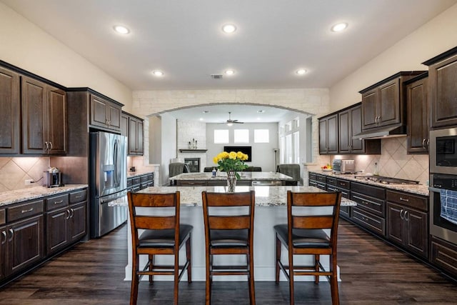 629 Asher Ct, Leander, TX 78641 - kitchen featuring appliances with stainless steel finishes, ceiling fan, open floor plan, a breakfast bar area, and arched walkways