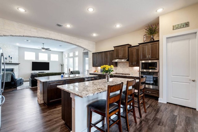 629 Asher Ct, Leander, TX 78641 - kitchen with stainless steel appliances, an island with sink, ceiling fan, dark brown cabinetry, and dark wood-type flooring
