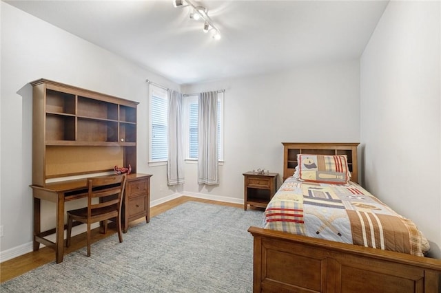 bedroom featuring wood finished floors, rail lighting, baseboards, and a desk