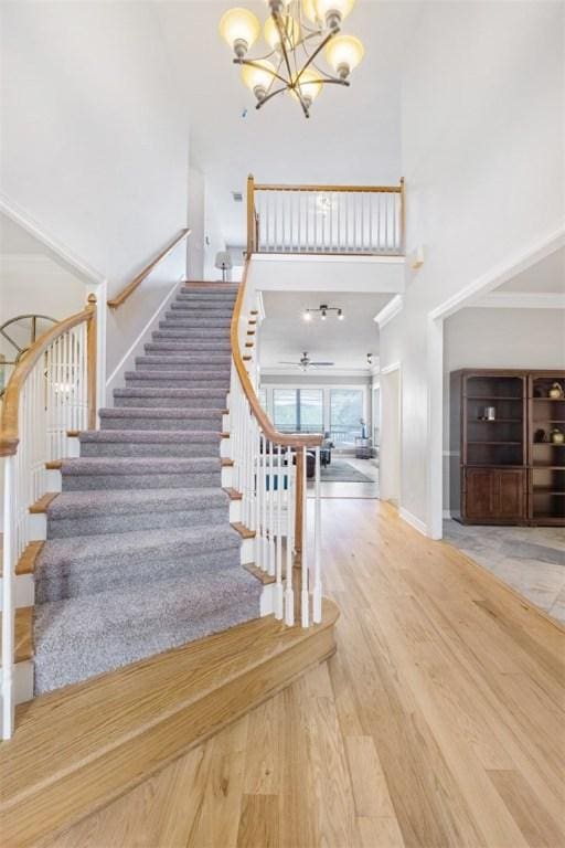 stairway featuring a towering ceiling, a chandelier, wood finished floors, a ceiling fan, and baseboards