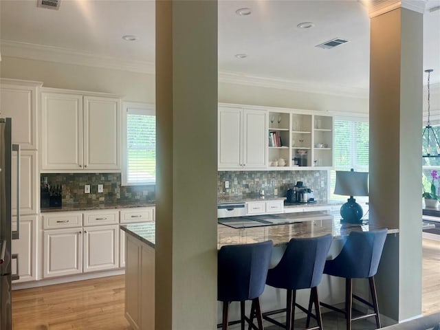 kitchen featuring tasteful backsplash, dark stone counters, white cabinets, a breakfast bar area, and crown molding