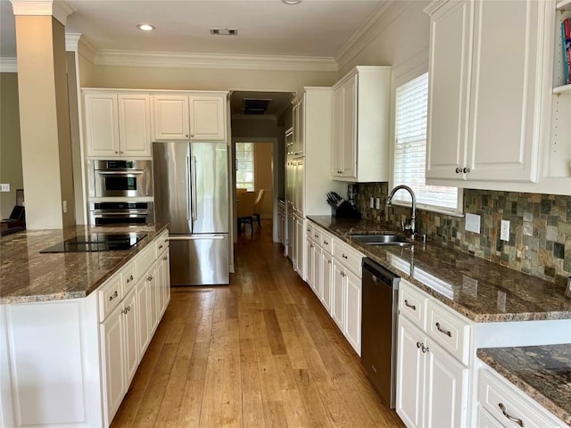kitchen featuring appliances with stainless steel finishes, a sink, light wood-type flooring, white cabinets, and ornamental molding