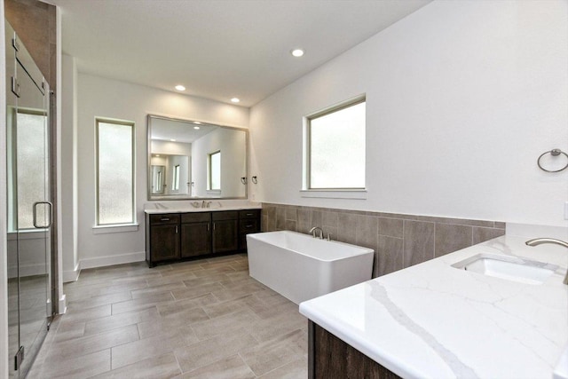 bathroom with two vanities, a soaking tub, wainscoting, and a sink