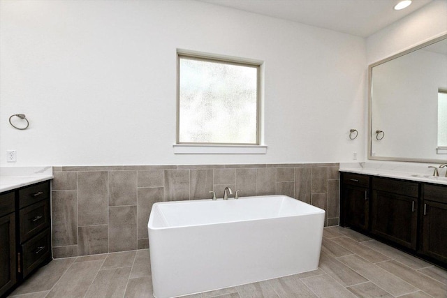 bathroom featuring a freestanding bath, tile walls, a wainscoted wall, and vanity