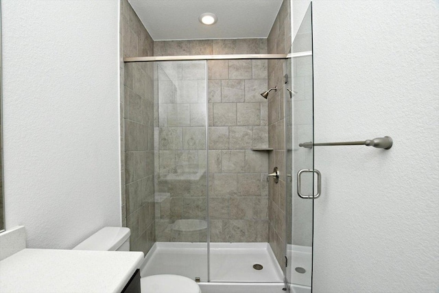 bathroom with toilet, vanity, a textured wall, and a stall shower