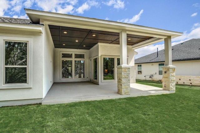 rear view of property with stucco siding, a lawn, and a patio