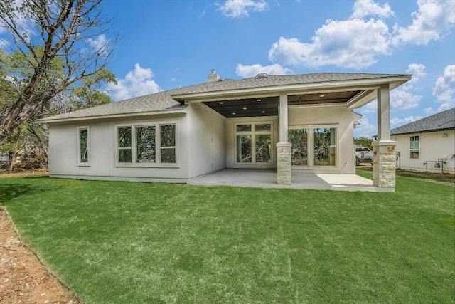 rear view of house featuring a shingled roof, a patio area, and a lawn